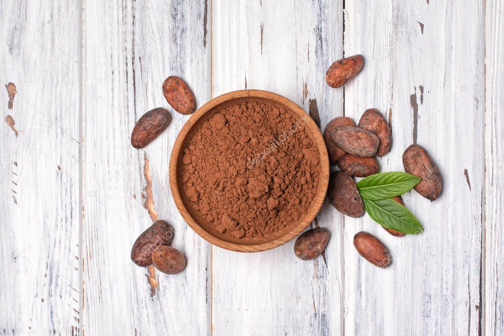 Cocoa beans and powder in bowl with green leaves
