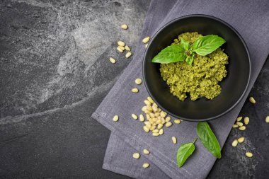 Kopya alanı ile siyah mermer arka plan üzerinde çam fıstığı ve fesleğen yaprakları gibi malzemelerle kasede pesto sos üst görünümü