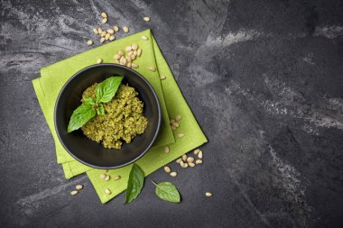 Kopya alanı ile yeşil keten peçete ve siyah mermer arka plan üzerinde fesleğen yaprakları ile kase de pesto sos üst görünümü