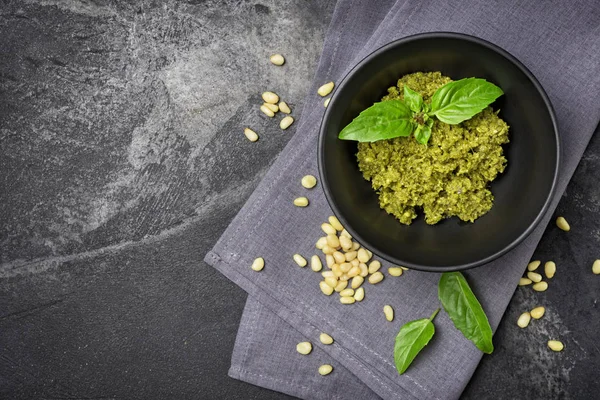Kopya alanı ile siyah mermer arka plan üzerinde çam fıstığı ve fesleğen yaprakları gibi malzemelerle kasede pesto sos üst görünümü