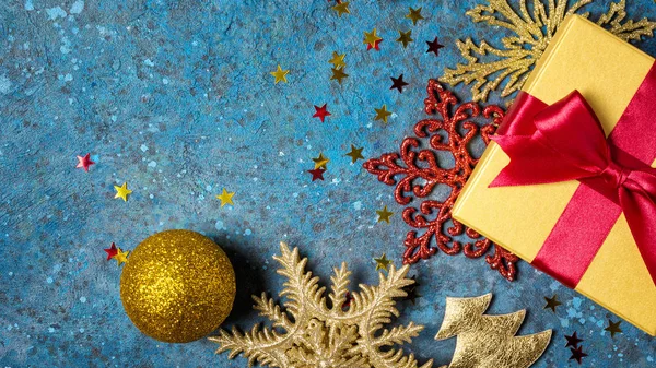 Zlatá dárková krabička s lesklým červeným saténovým lukem s vánoční ozdobou — Stock fotografie