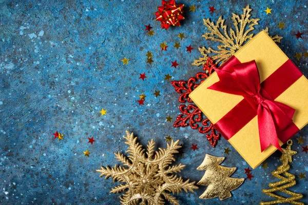Zlatá dárková krabice s lesklou červenou saténovou mašlí a vánoční ozdobou — Stock fotografie