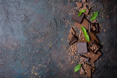 Kırık süt ve koyu çikolata parçalarının üst görüntüsü. Kahverengi beton zemin üzerinde taze yeşil nane ve fotokopi alanı var.