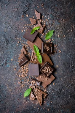 Kırık sütün ve kahverengi beton arka planda taze yeşil naneli koyu çikolataların üst görüntüsü.