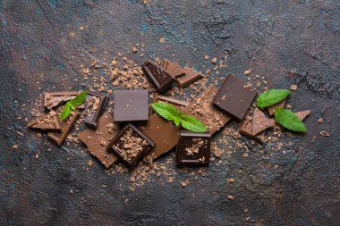 Kırık sütün ve kahverengi beton arka planda taze yeşil naneli koyu çikolataların üst görüntüsü.