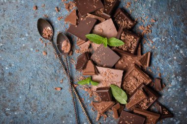 Kırık süt ve taze yeşil naneli siyah çikolata ve mavi beton arka planda iki uzun kokteyl kaşığı.