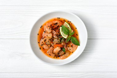 Turuncu Asya soslu baharatlı karidesli kâse manzarası. Beyaz ahşap arka planda siyah susam tohumları.