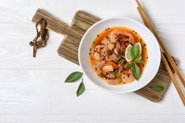 Turuncu Asya soslu baharatlı karidesli, ahşap tahtada ve beyaz ahşap arka planda limon ve siyah susam tohumlu kâse manzarası.