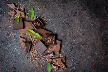 Kırık süt ve koyu çikolata parçalarının üst görüntüsü. Kahverengi beton zemin üzerinde taze yeşil nane ve fotokopi alanı var.
