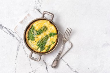 Yeşil ıspanak yapraklı, ahşap tahtada çatal ve fotokopi alanı olan beyaz mermer arka planlı lezzetli omlet manzarası.