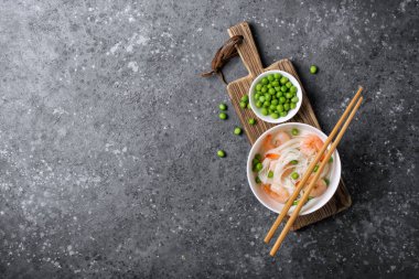 Çin pilavlı erişte, lezzetli karidesler, yeşil bezelyeler ve gri beton arka planda tahta çubuklar ve fotokopi alanı olan en iyi kase manzarası.