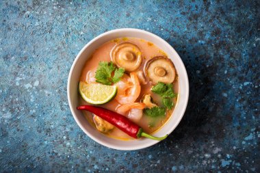 Tom Yam domates çorbası, lezzetli karidesler, midyeler, şiitake mantarları, kireç ve kırmızı biberli mavi beton arka plan.