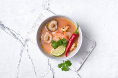 Tom Yam domates çorbası, lezzetli karidesler, midyeler, şiitake mantarları, kireç, ahşap tahtada kırmızı biber ve beyaz mermer arka plan.