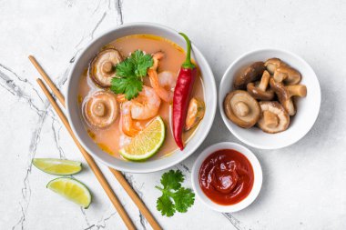 Tom Yam domates çorbası, lezzetli karidesler, midyeler, şiitake mantarları, limon, acı biber ve ahşap çubuklar beyaz mermer arka planda.