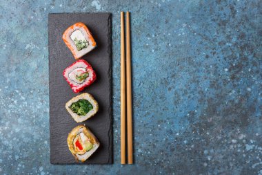 Geleneksel Japon yemeklerinin en üst görüntüsü parlak lezzetli suşi somon, havyar, avokado ve krem peynirle birlikte mavi beton arka planda fotokopi alanı ile yuvarlanıyor.