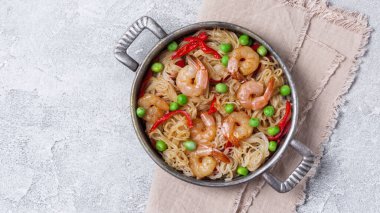 Çin pilavlı erişteli tava, lezzetli karidesler, yeşil bezelyeler ve gri beton arka planda kırmızı biber.