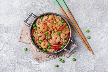 Çin pilavlı erişteli tava, lezzetli karidesler, yeşil bezelyeler ve gri beton arka planda kırmızı biber.