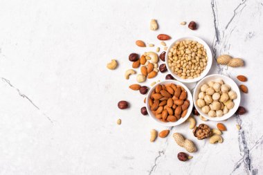 Üç kâse badem, fındık, ceviz, fıstık, fındık ve çam fıstığı beyaz mermer arka planda fotokopi alanı