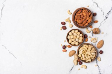 Badem, fındık, ceviz, fıstık, fındık ve çam fıstığı içeren beyaz mermer arka planda fotokopi alanı olan kaselerin üst görüntüsü.