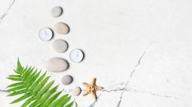 Spa konsepti. Beyaz mermer zemin üzerinde gri deniz taşlarının ve aroma mumlarının üst görüntüsü.