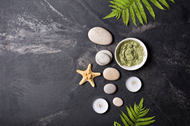 Spa ve güzellik konsepti. Gri deniz taşlarının üst görünümü, kozmetik kil ve aroma mumları siyah mermer zemin üzerinde kopya alanı ile
