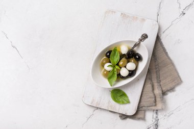 Lezzetli, yeşil ve siyah zeytinlerin karışımı mozzarella, fesleğen yaprakları beyaz ahşap tahtada ve mermer arka plan ve fotokopi alanı