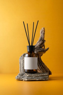 Aroma yayıcı kahverengi cam şişede ve turuncu arka planda dallar ve sürüklenen dallar, doğal dokular ve sağlıklılık kavramı ile minimalist natüralist yaşam.