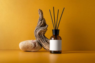 Aroma yayıcı kahverengi cam şişede taş podyumda, sopalarla, dallarla ve turuncu arka planda, minimalist natüralistlerin doğal dokuları ve sağlıklı yaşam konseptiyle..