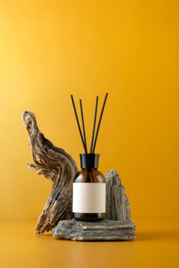 Aroma yayıcı kahverengi cam şişede taş podyumda, sopalarla, dallarla ve turuncu arka planda, minimalist natüralistlerin doğal dokuları ve sağlıklı yaşam konseptiyle..