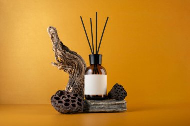 Aroma yayıcı kahverengi cam şişe çubuklar, sürüklenen odun ve kurutulmuş nilüfer tohumları turuncu arka planda, minimalist natüralist doğal dokular ve refah konsepti ile yaşam.