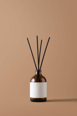 Kehribar cam kamış ayırıcı ve bej arka planda boş etiket. Markalaşma, lüks kaplıca, parfüm tasarımı, organik güzellik ve sağlık yaşam tarzı kavramları için minimalist aroma terapisi..