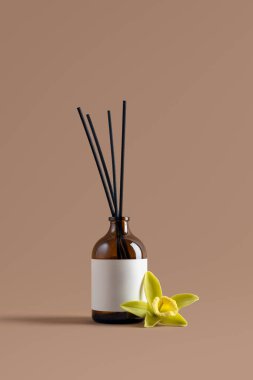 Kehribar cam kamış ayırıcı, üzerinde boş etiket ve bej arka planda vanilyalı orkide çiçeği var. Markalaşma, lüks spa, sağlık ve organik tasarım için minimalist aromaterapi ve parfüm modeli.
