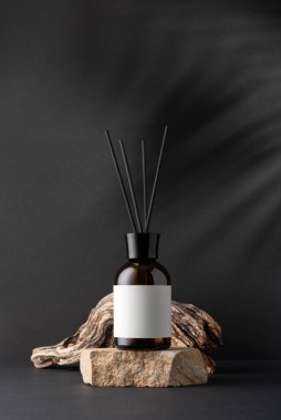 Kahverengi cam aroma yayıcı, kamış çubukları ve siyah arka planda sürüklenen ağaç dalları, minimalist durgun yaşam bileşimi, doğal dokular ve sağIık kavramı.