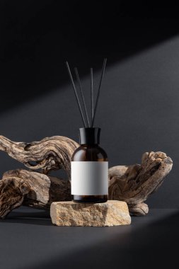 Kahverengi cam aroma yayıcı, kamış çubukları ve siyah arka planda sürüklenen ağaç dalları, minimalist durgun yaşam bileşimi, doğal dokular ve sağIık kavramı.