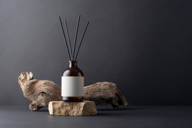 Kahverengi cam aroma yayıcı, kamış çubukları ve siyah arka planda sürüklenen ağaç dalları, minimalist durgun yaşam bileşimi, doğal dokular ve sağIık kavramı.
