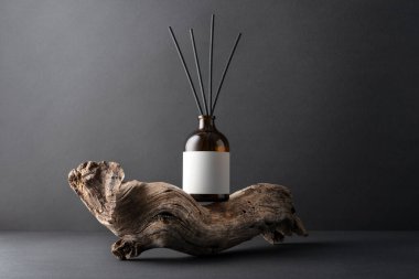 Kahverengi cam aroma yayıcı, kamış çubukları ve siyah arka planda sürüklenen ağaç dalları, minimalist durgun yaşam bileşimi, doğal dokular ve sağIık kavramı.