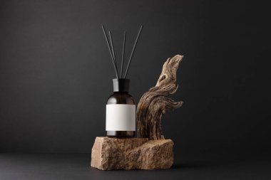 Kahverengi cam aroma yayıcı, kamış çubukları ve siyah arka planda sürüklenen ağaç dalları, minimalist durgun yaşam bileşimi, doğal dokular ve sağIık kavramı.