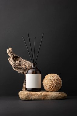 Siyah arka planda kahverengi cam aroma yayıcı, sürüklenen ağaç dalları ve taş küre, minimalist natüralist natürmort yaşam bileşimi, doğal dokular ve sağlık konsepti.