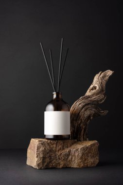 Kahverengi cam aroma yayıcı, kamış çubukları ve siyah arka planda sürüklenen ağaç dalları, minimalist durgun yaşam bileşimi, doğal dokular ve sağIık kavramı.