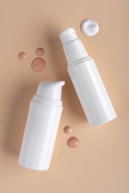 Beyaz tüpler, krem damlaları ve bej arka planda fondöten ile minimal kozmetik kompozisyon. Cilt bakımı, güzellik, makyaj ve sağlık kavramları için mükemmel..