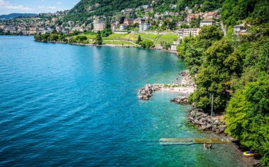 Veytaux 'daki Cenevre Gölü kıyı şeridinin en üst manzarasında yüzen insanlar ve Vaud İsviçre' deki Montreux şehri var.