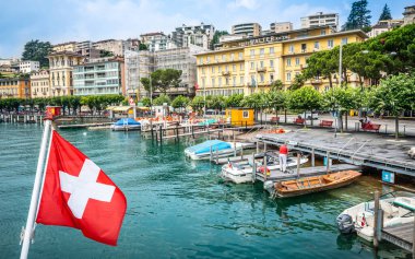 Lugano İsviçre, 1 Temmuz 2020: İsviçre bayrağı ve Lugano şehri Lugano Ticino Gölü kıyısında