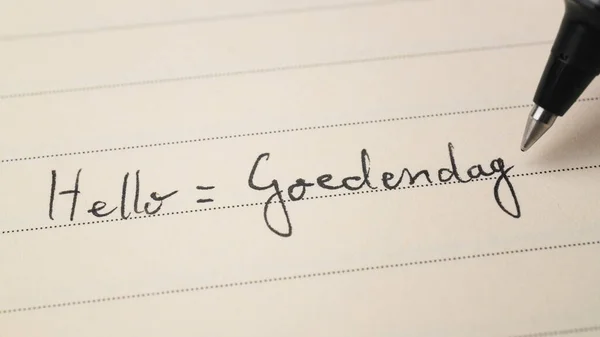 Beginner Dutch language learner writing Hello formal word Goedendag for homework on a notebook macro shot