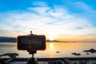 Akıllı telefon kamera tropikal deniz ve dağ üzerinde akşam günbatımı manzara fotoğrafçılığı tripod stand. Fotoğraf doğal peyzaj günbatımı ve gündoğumu mavi gökyüzü arka plan ile cep telefonu alarak.