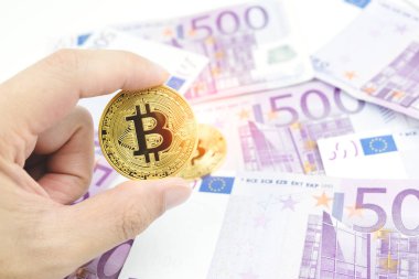 Altın bitcoin bulanık beş yüz euro banknot arka plan üzerinde tutan adam el kapatın. Cryptocurrency, euro para faturaları ile dijital para.