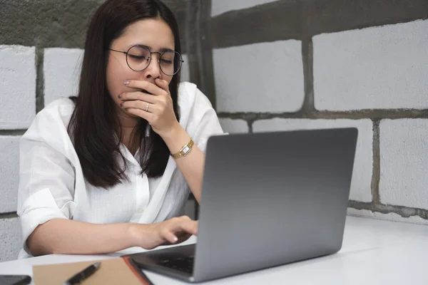 疲惫的昏昏欲睡的商业妇女在眼镜打呵欠 而使用笔记本电脑在办公桌工作到深夜 无聊的学生在晚上的电脑阅读演示准备考试 过度劳累 — 图库照片