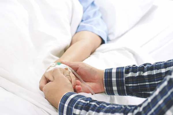 Kadın hasta el güven verici ve teşvik karısı için hastanede yatağında intravenöz enjeksiyonla serum fizyolojik çözüm alma tutan adam el. Tıbbi tedavi, sağlık, Aile ve sevgi kavramı.
