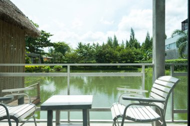Beyaz ahşap masa ve sandalyeler beyaz çelik çit ve sabah parlayan güneş evi ve göl manzaralı bir teras bulunur. Balkon oturma gevşeme için.