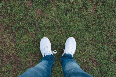 Erkek kot pantolon ve üstten görünüm çim üzerinde duran beyaz spor ayakkabı ayakkabı giyer.