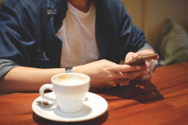 Vintage sesi kafede kahve ile akıllı telefon kullanan genç hipster adam. El bekle kapatın ve online banka için hareket eden telefon ekranında dokunuyor, mesajı okumak, arkadaşlarınızla sohbet, sms göndermek.
